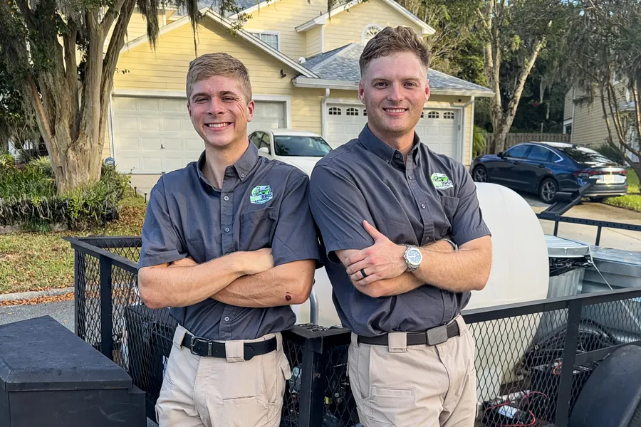 Dakoda and Austin Hill of Hill Bros Bin Cleaning in uniform in front of their bin cleaning trailer in a Jacksonville neighborhood